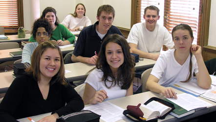 Students at tables in a classroom smiling at the camera