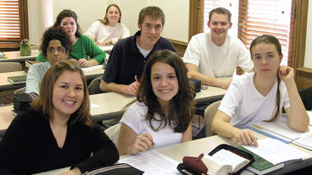Young adult students at their desks smiling at the camera
