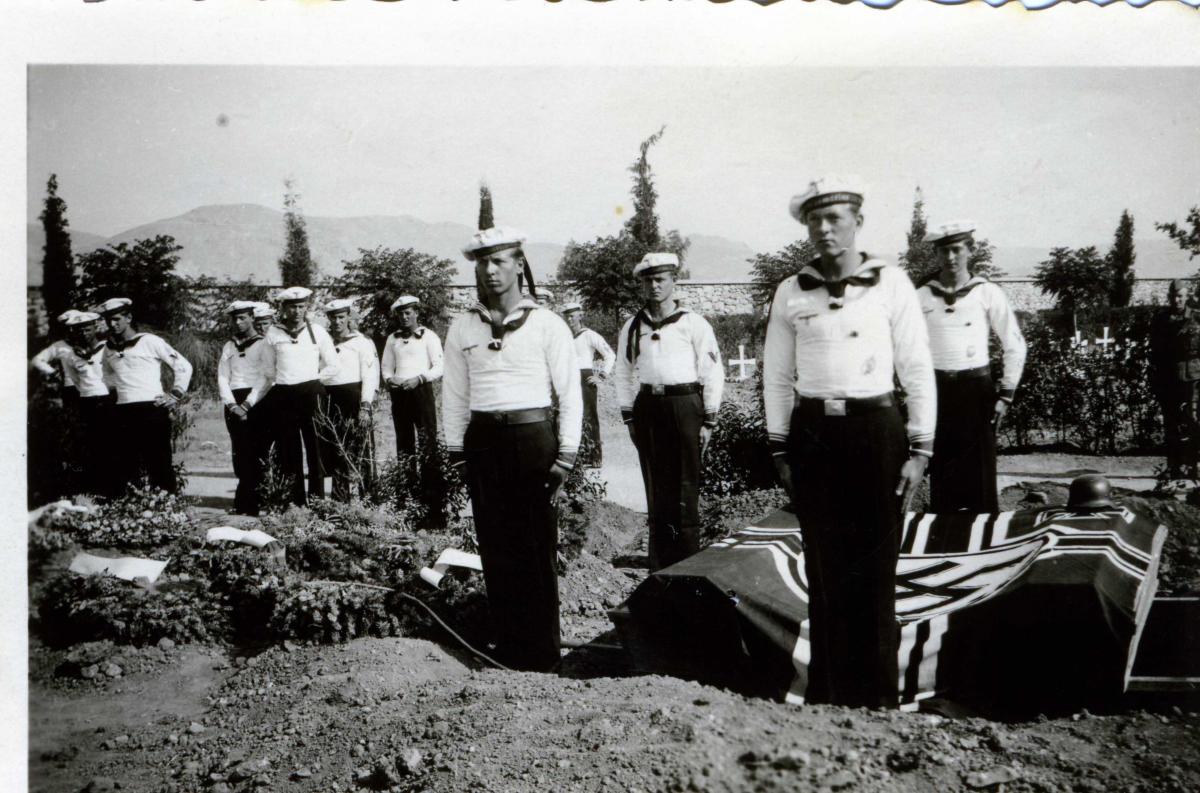 Sailors standing erect in grave yard wit Nazi flag covering caskets