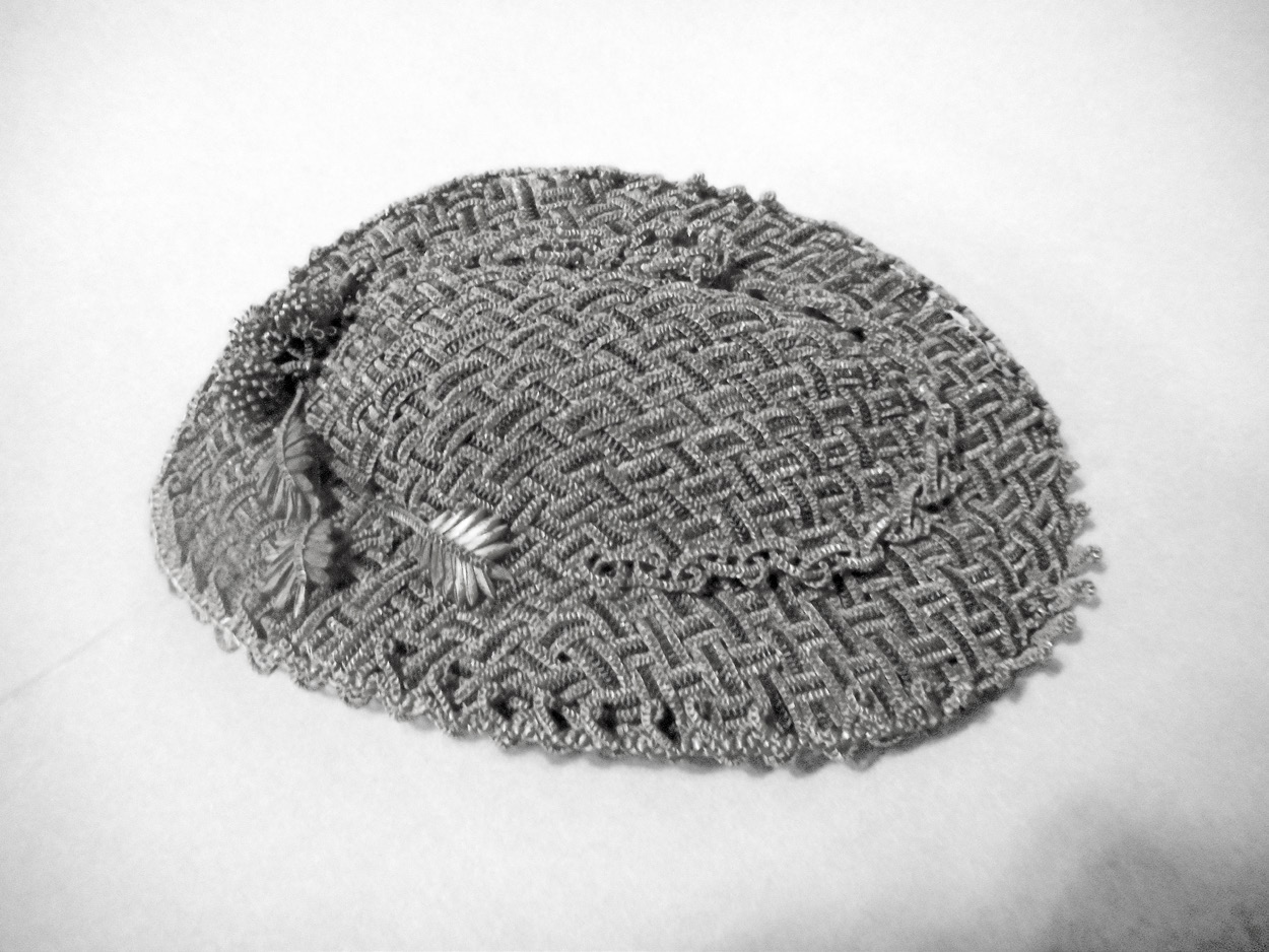 A small exquisite flat hat, an apparent adaptation of the Fanchon and Bergere styles, popular in the 1860s. The size of the cut straw is minute, three braids per strand, two colors per strand, woven and sewn together to cover the frame, and then trimmed with a single strand of braided light straw, several straw blossoms and straw leaves. The donor is unknown. LDS 40–323–1 Church History Museum.