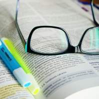 A pair of glasses and two highlighter pens on an open book of scripture