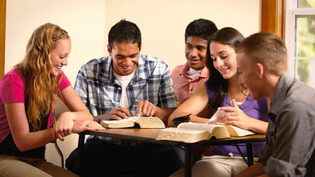 Several young people gathered around a table to study the scriptures