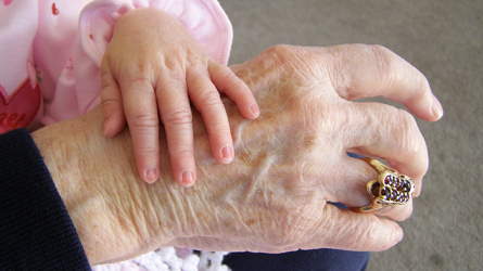 A child's hand placed on a grandparent's hand