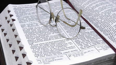 A pair of reading glasses perched atop an open Bible