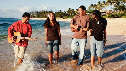 Youth walking along a beach playing music and laughing together