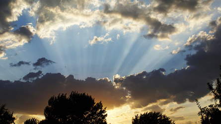 Rays of sunlight shining through a cloud-streaked evening sky