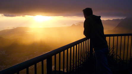 A lone person looks at the setting sun from a balcony