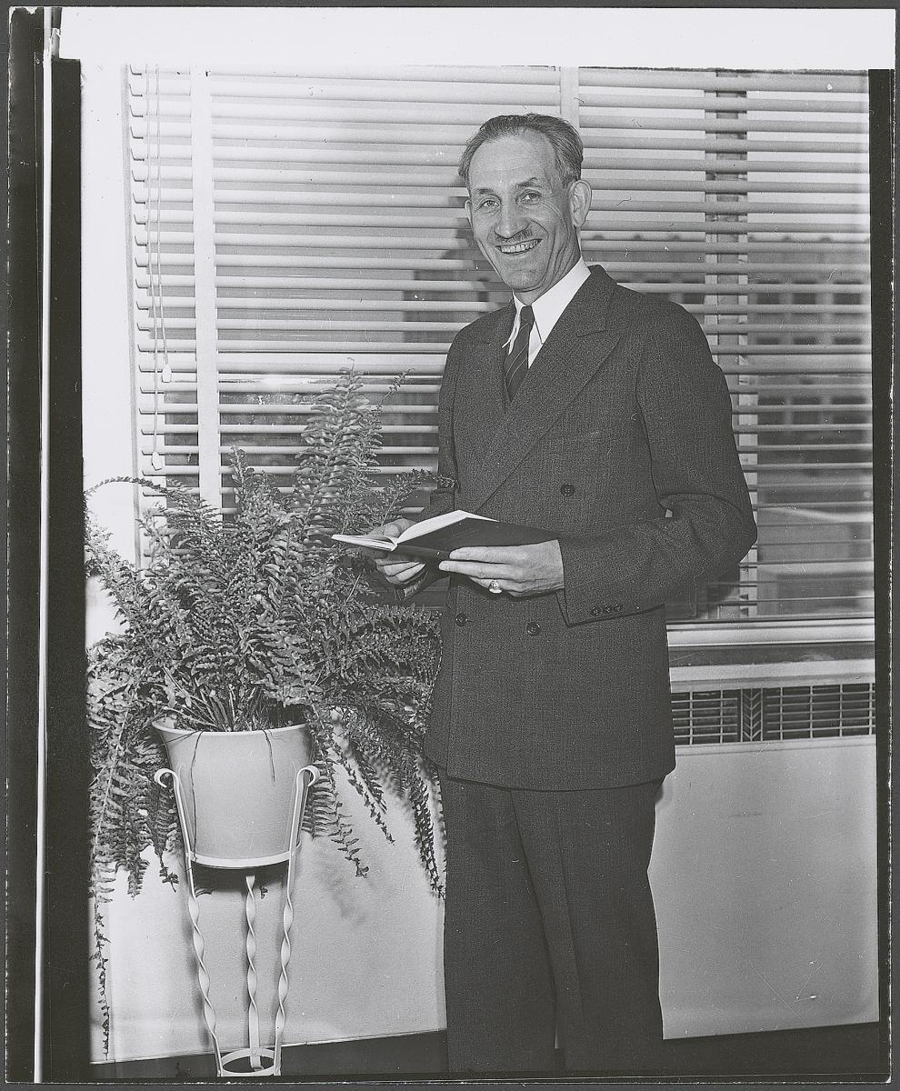 J. Wyley Sessions standing by window holding open book