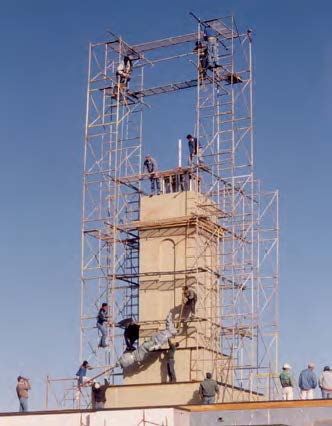With no crane to assist them, workmen hoist the wrapped angel to the top of the temple’s tower