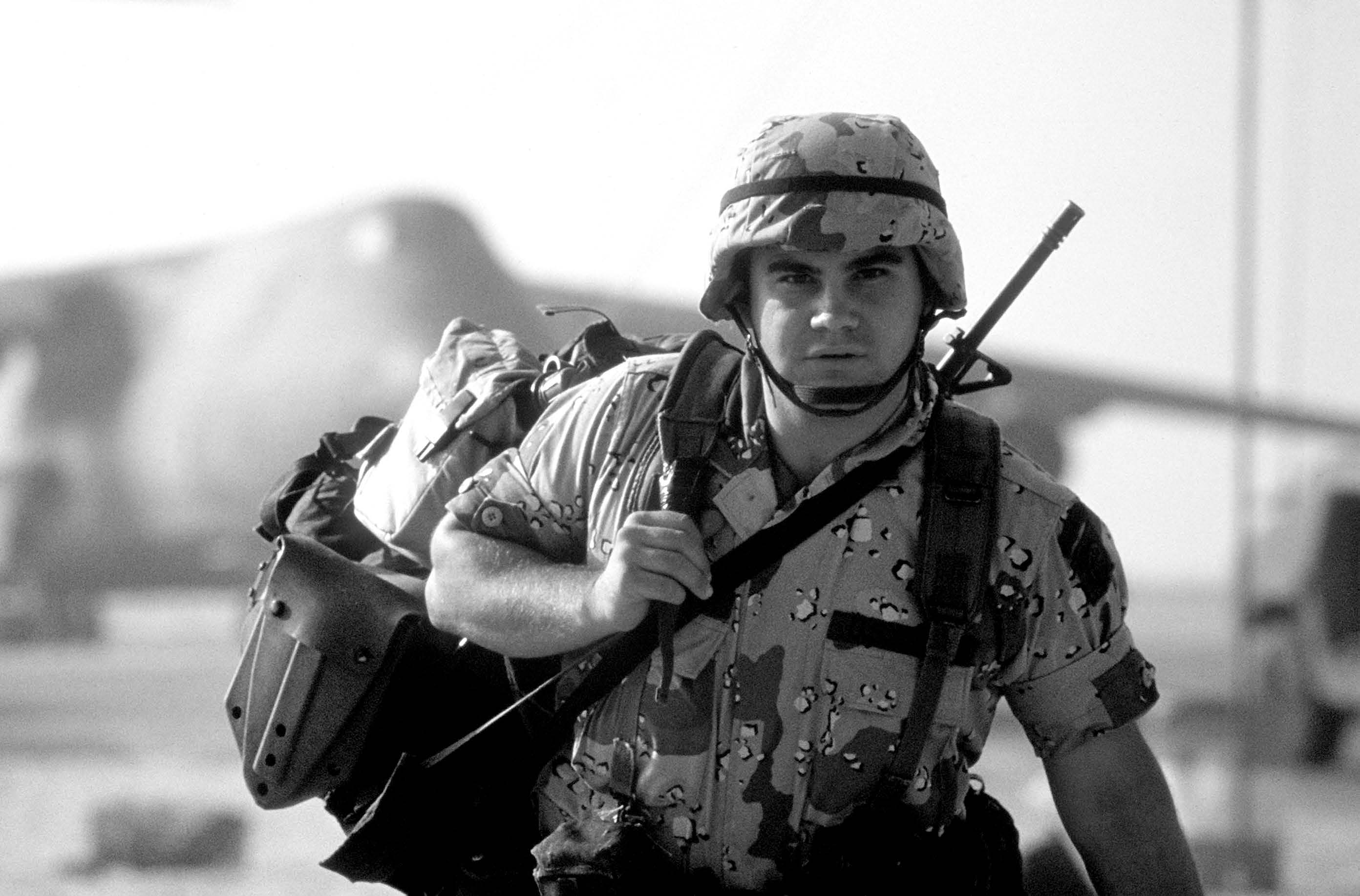 A soldier carries his gear after arriving in Saudi Arabia during Operation Desert Shield. Courtesy of DoD.