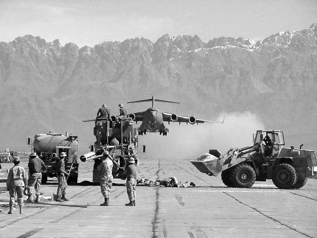 An American C-17 aircraft is shown taking off over the heads of soldiers from the 92nd Engineer Battalion. Soldiers are shown repairing the base runway in March 2002. Note the rugged mountains in the background. Courtesy of Stephen C. Larsen.