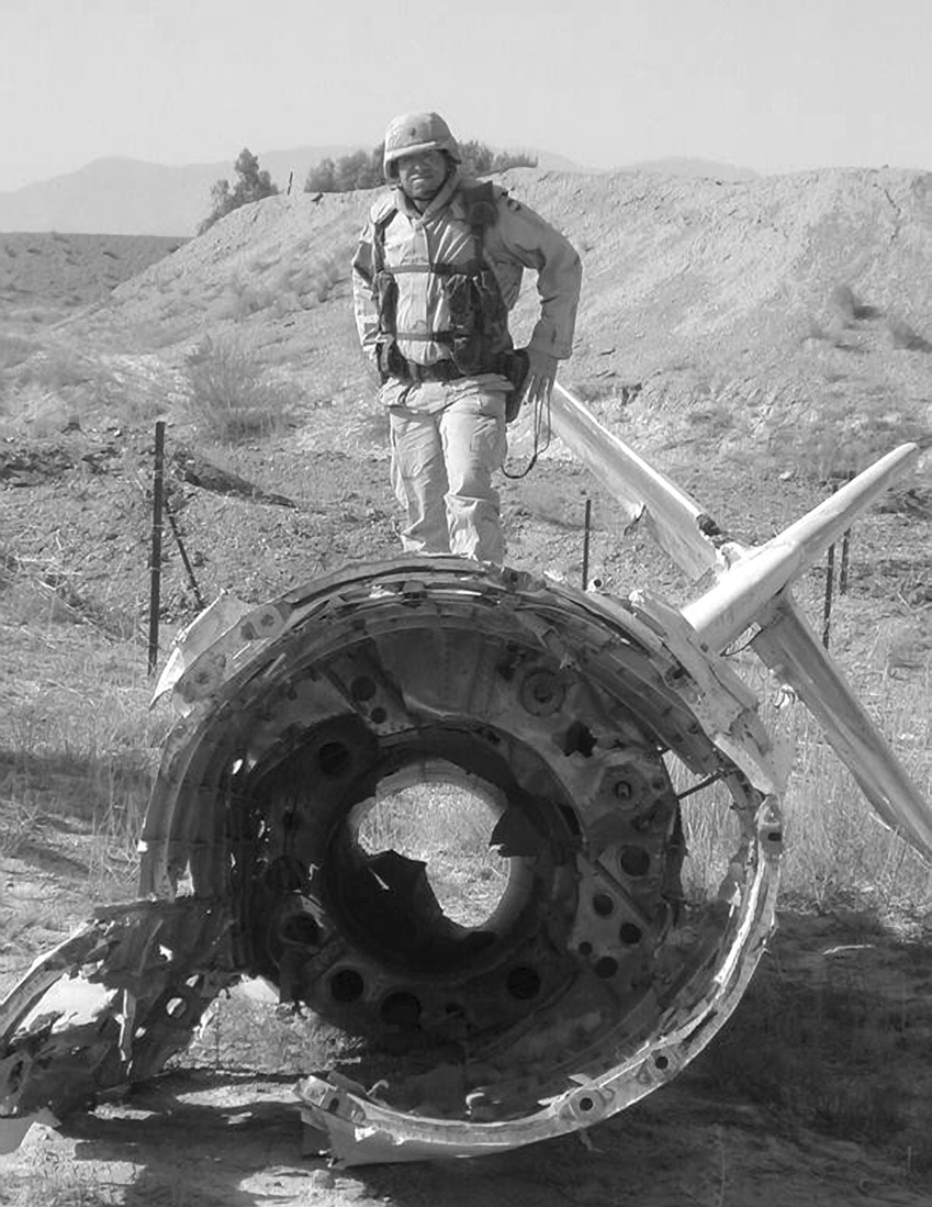 Lieutenant Colonel Stephen C. Larsen, in full battle gear, is standing on the tail of a wrecked Afghan MiG aircraft in January 2002 at Kandahar, Afghanistan. Courtesy of Stephen C. Larsen.