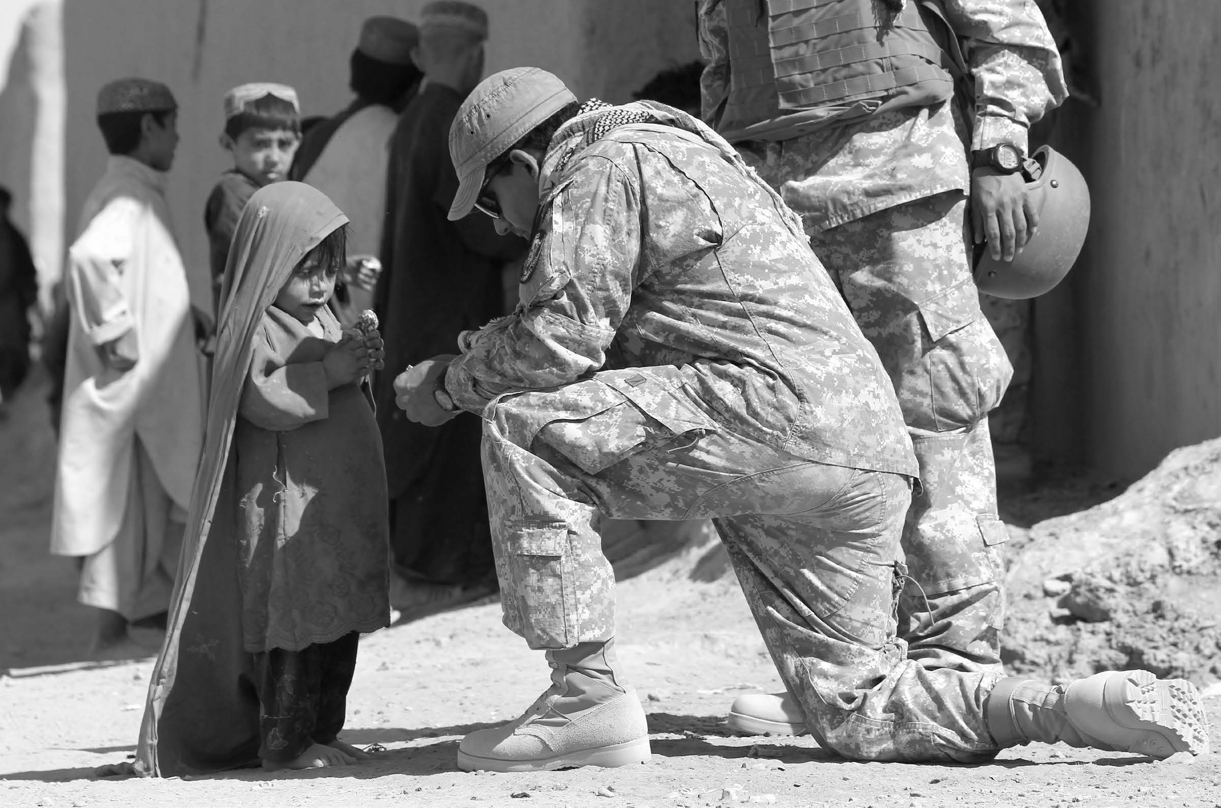 An American soldier kneels to give a lollipop to an Afghan child. Courtesy of J. Joseph DuWors.