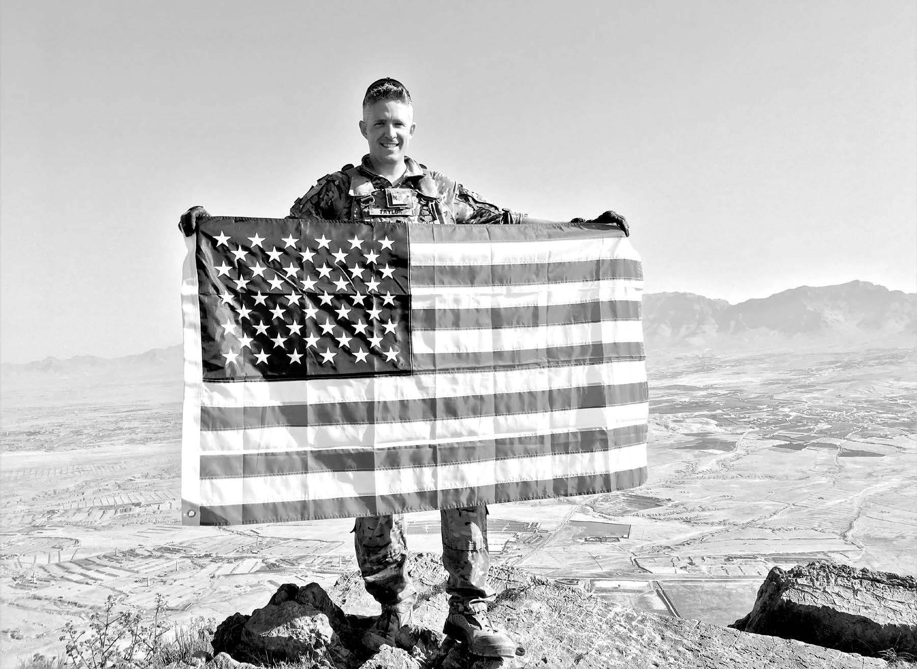 Major Brent Taylor unfurling an American flag on a mountain top in Afghanistan during the summer of 2018. Courtesy of Jennie A. Taylor.