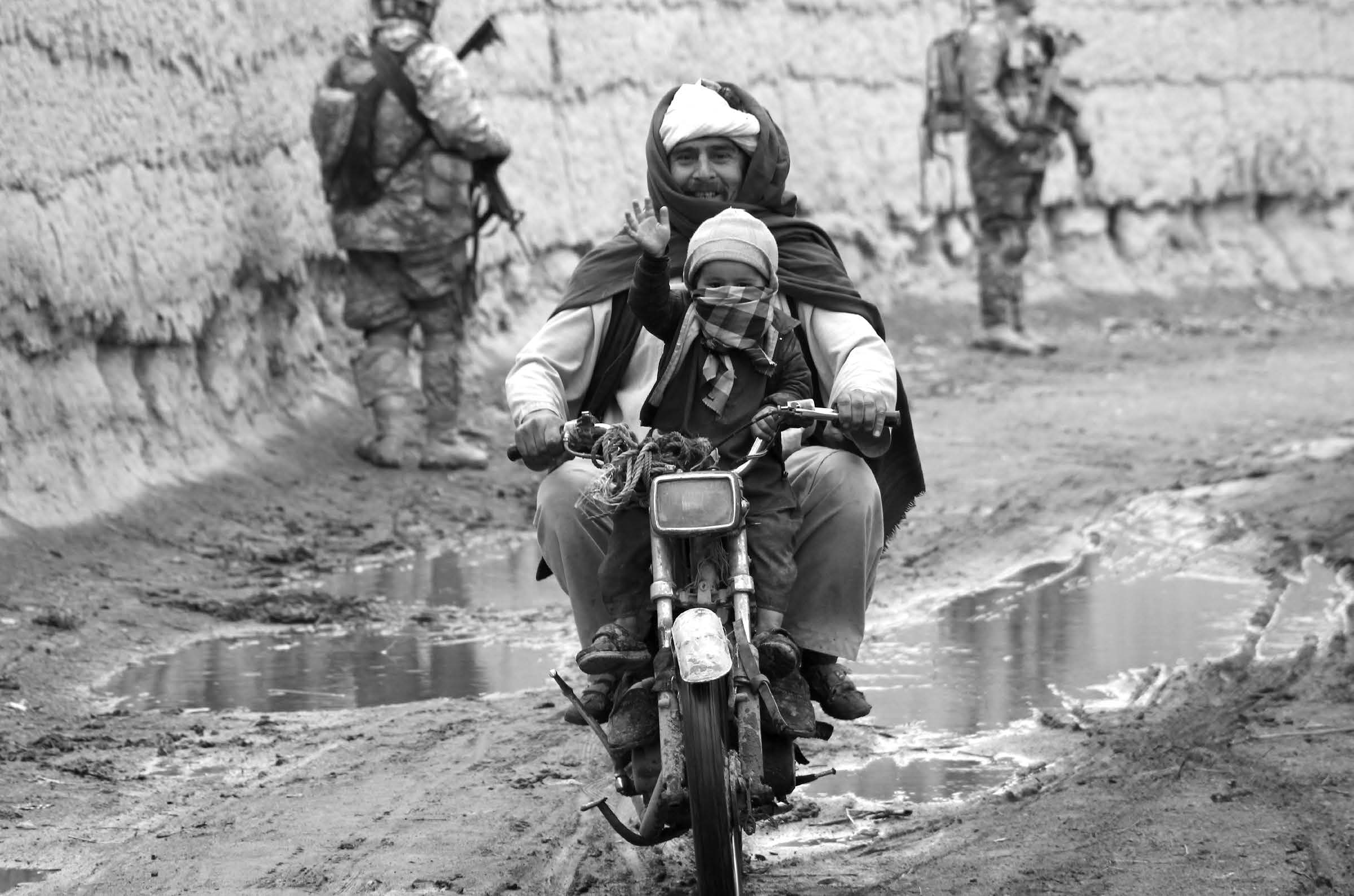 With American soldiers on patrol behind him, an Afghan father and his son pass through their lines. Courtesy of J. Joseph DuWors.