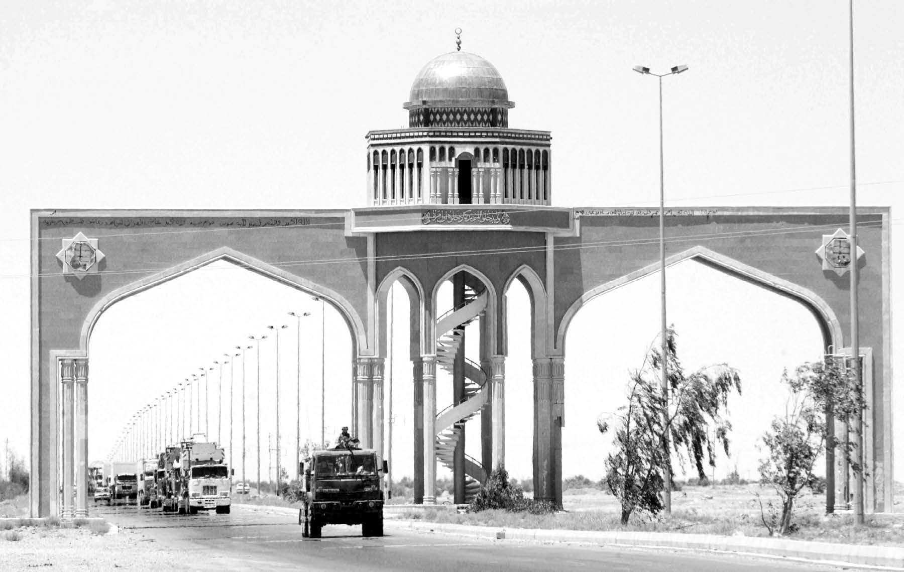 A gun truck from an air expeditionary force transportation company moves under an archway on the Main Supply Route with a convoy in tow in June 2004. Courtesy of DoD.