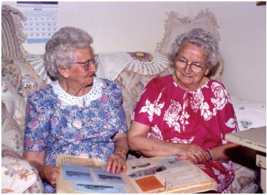 Two elderly sisters looking at a book