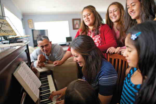 photo of a large family gathered around a piano to sing together