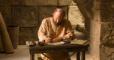 An Apostle sitting at a table writing on manuscript pages